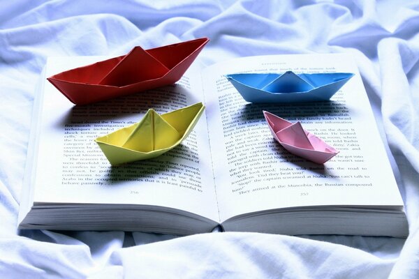 Barcos de papel de colores en el fondo de un libro abierto