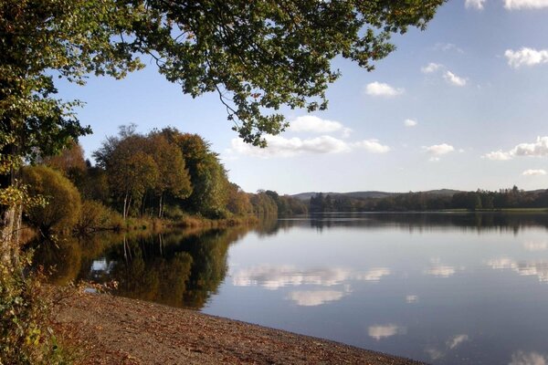 Orilla del lago de otoño con el reflejo de las nubes en el lago