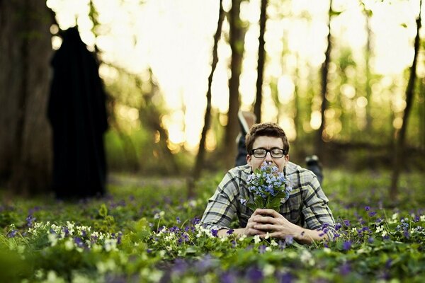 Mann liegt auf einer Lichtung im Wald mit einem Blumenstrauß