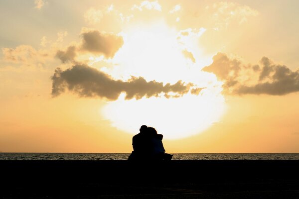 Para przytulanie siedzi na tle zachodu Słońca na morzu