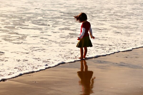 Chica moja sus pies en el agua en la playa