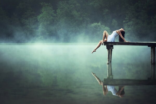 A girl is resting on a bridge over the surface of the lake