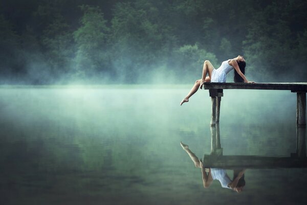 Una niña descansa en un puente sobre la superficie del lago