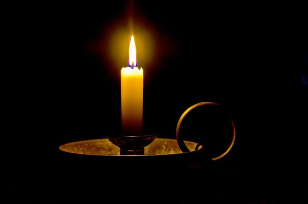 A candle burns in a candlestick on a black background