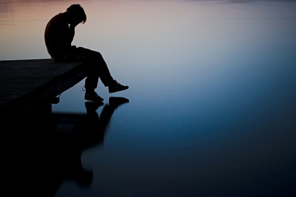 Der Junge, der am Pier am Fluss sitzt, sehnt sich danach