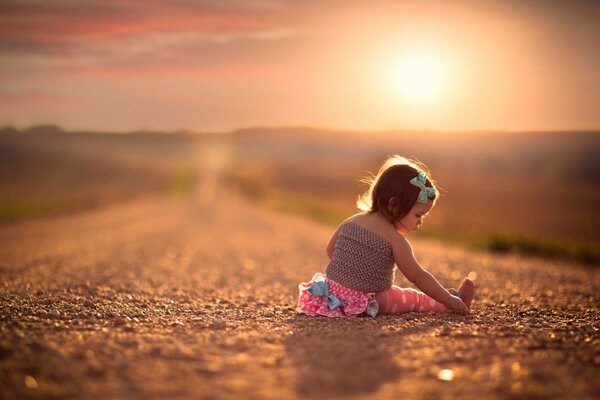 A little girl is sitting on the road in the sunset light