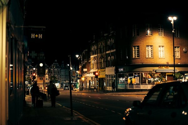 Persone che camminano sul marciapiede e passano accanto alle auto lungo la strada a Londra alla luce della sera