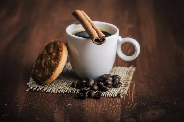 Sur une table en bois, une tasse blanche avec du café, de la cannelle, du foie et des grains de café