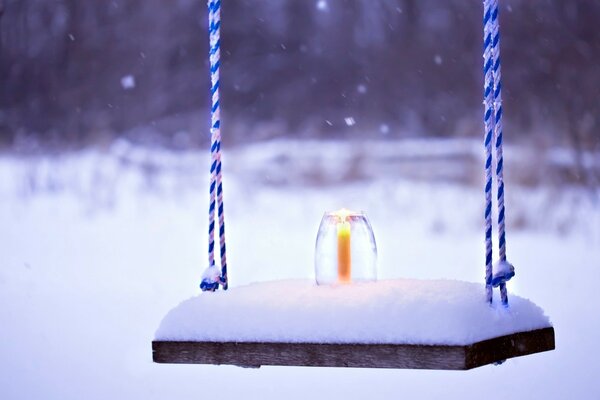 Snowy landscape, swing in the snow, burning candle in the snow