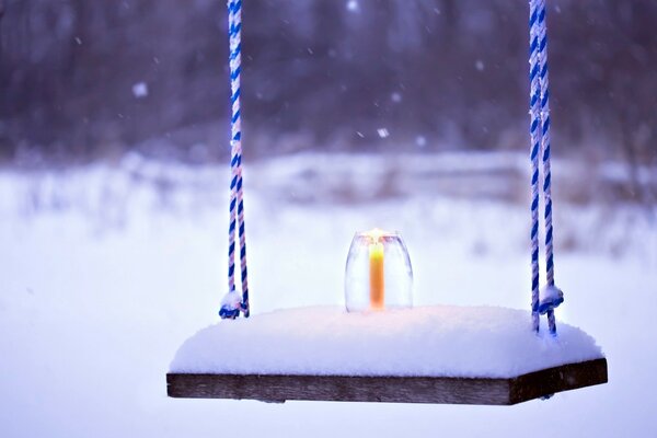 Снежный пейзаж, качели в снегу, горящая свеча на снегу