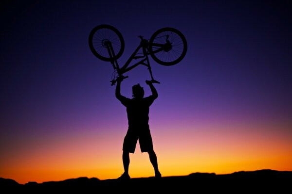 Mężczyzna podniósł rower na tle zachodu słońca, piękne niebo