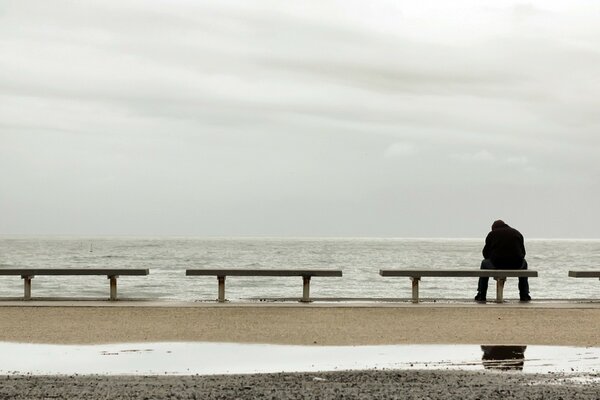Uomo seduto da solo in riva al mare su una panchina