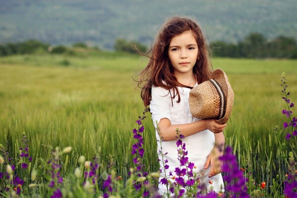 A girl among purple flowers holds a hat