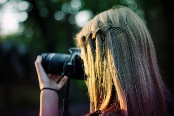 A blonde girl takes pictures of nature with hairpins and a braided pigtail