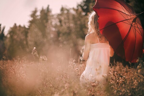 Mädchen in einem weißen Kleid und mit einem roten Regenschirm unter den Blumen