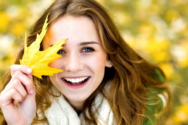 Chica positiva cubre su cara con una hoja de otoño