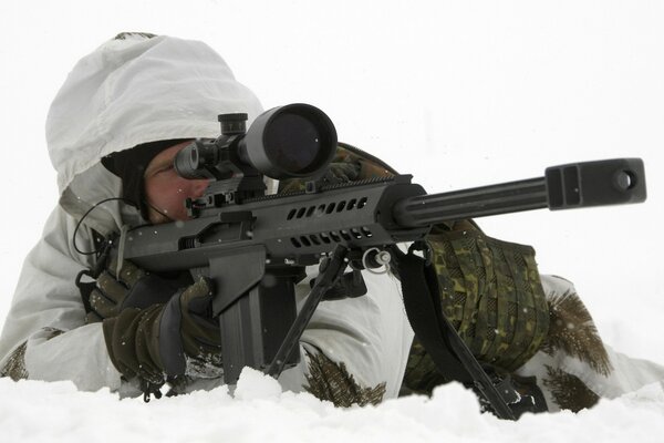 A soldier with a machine gun lying in the snow