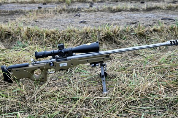 A sniper rifle stands on a tripod on the grass in a field