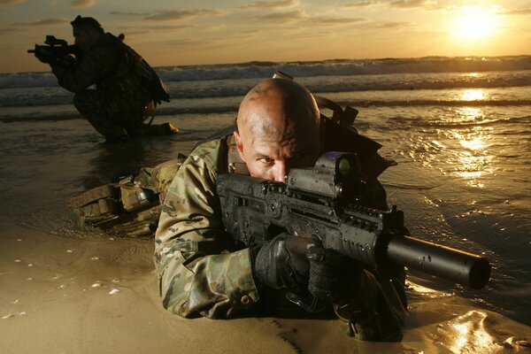 Soldado con armas en la orilla del mar al atardecer