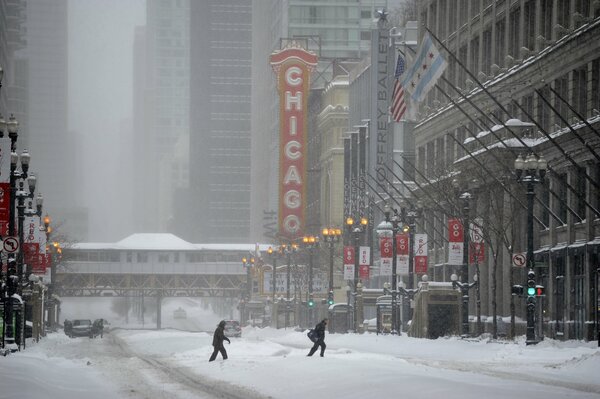 Люди переходят заснеженную улицу зимнего Чикаго