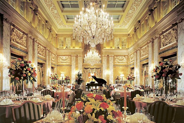 A hall with tables decorated with bouquets, crystal chandeliers and a black grand piano