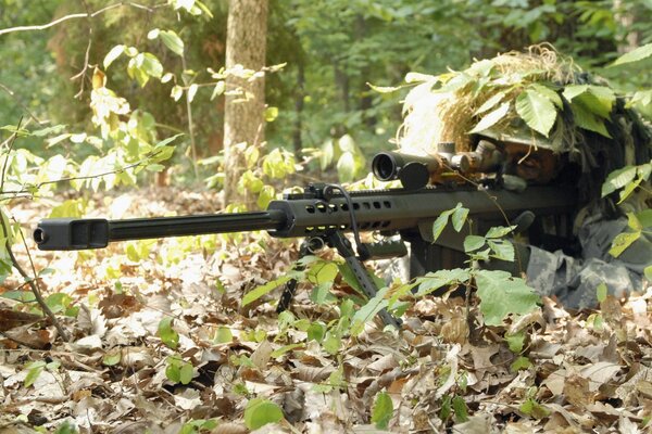 Francotirador con rifle en el bosque al camuflaje