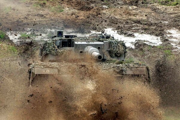 Tank vor dem Hintergrund des Feldes und des fliegenden Staubes