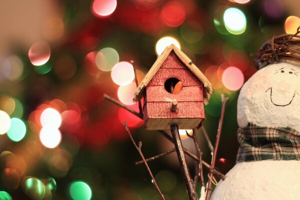 Schneemann hält ein Vogelhäuschen vor dem Hintergrund der Lichter