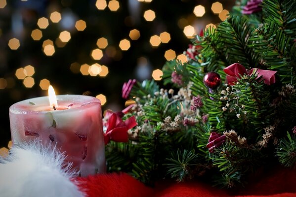 A burning candle next to a decorated Christmas tree