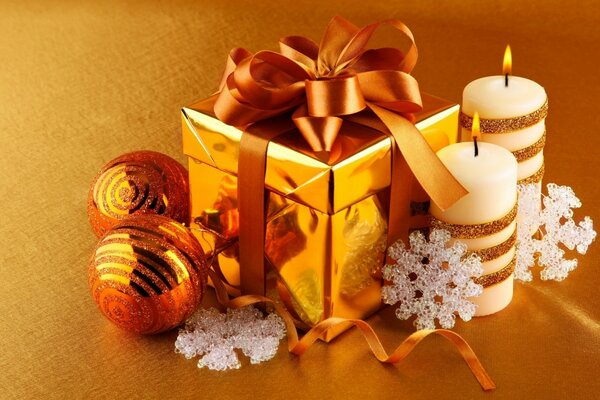 Рождественский подарок в золотистой коробке с лентой. Новогодние свечи на жёлтом фоне