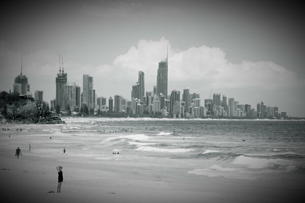 An ocean with high-rises on the shore and a cloudy sky above