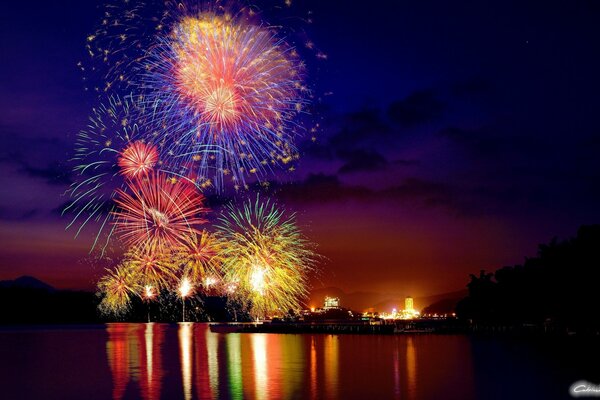 Fuegos artificiales elegantes sobre la ciudad y reflejos multicolores de la ciudad en la superficie Lisa del agua