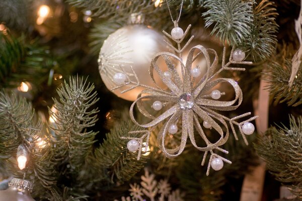 Eine Blume mit Perlen und eine Kugel auf einem mit Lichtern beleuchteten Weihnachtsbaum