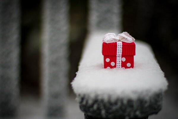 A cute little present on a snow-covered bench in the park. Red gift box