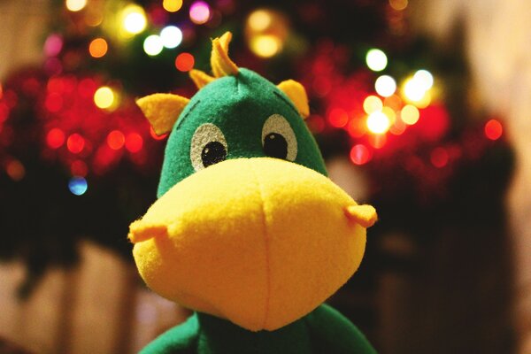 A toy green dinosaur on the background of a Christmas tree