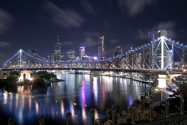 Glowing lights on the bridge. Houses and skyscrapers on the river of the night city