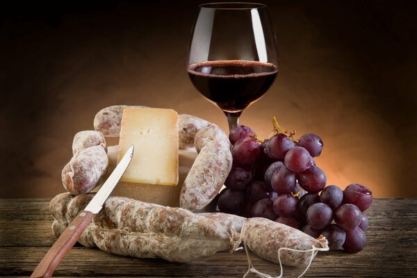 Red wine in a glass with a snack of cheese, sausage and grapes