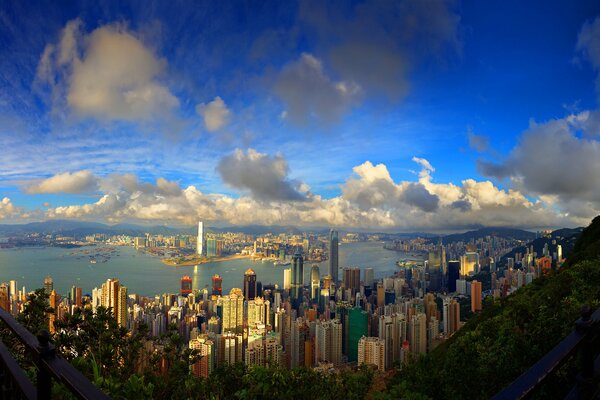 A metropolis with high-rise buildings against the background of water , mountains, the sky on which the sun is peeking