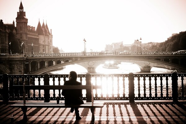 Schwarz-Weiß-Foto . Paris, Mann sitzt am Morgen auf einer Brücke auf einer Bank vor dem Hintergrund der Brücke , Häuser