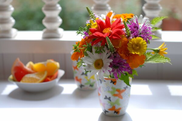 Blumenstrauß in einem Glas auf einer weißen Terrasse und eine Untertasse mit geschnittenen Früchten
