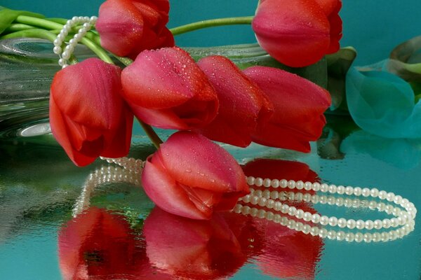 Czerwone tulipany owinięte naszyjnikiem z pereł leżą na błyszczącym stole