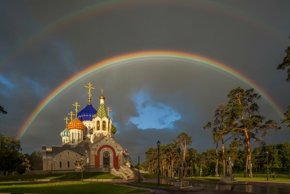 Double arc-en-ciel sur l église parmi les arbres