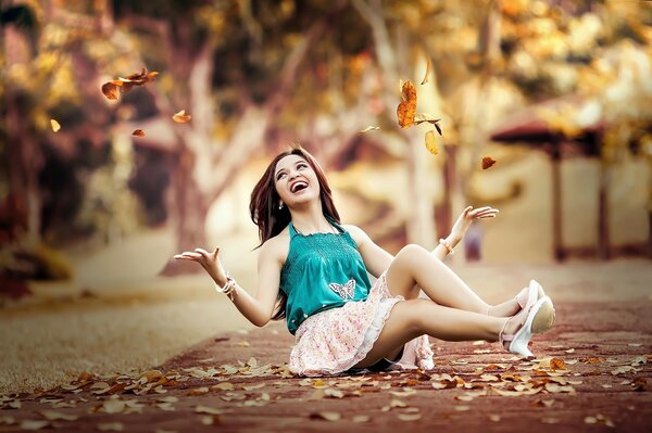 Jeune fille jette des feuilles assis sur le sol dans le parc