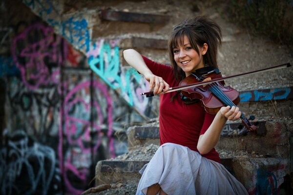 Lindsay Stirling playing the violin against a graffiti-covered staircase