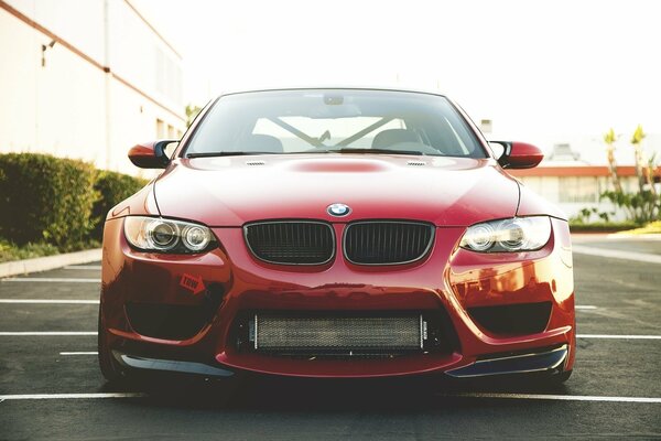 BMW rojo al lado del edificio en el estacionamiento