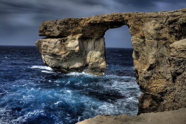 Arco di rocce nel mare blu, onde che battono contro le rocce