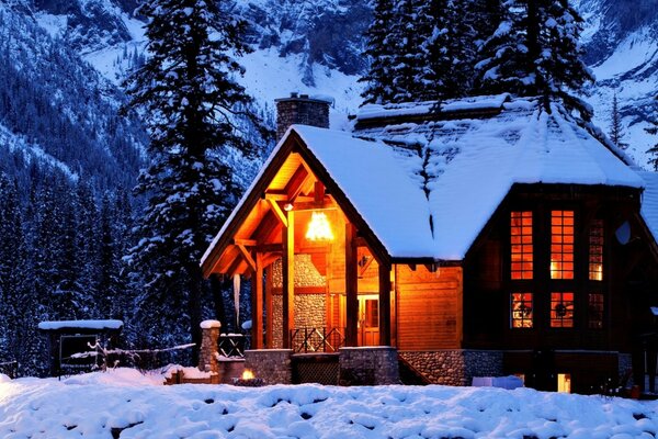 A snow-covered house next to trees in the mountains