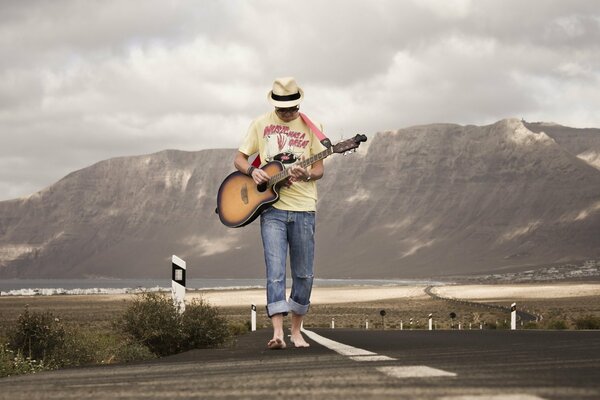 The guy is a guitarist walking along the road against the background of mountains