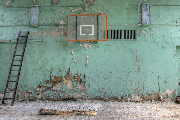 Opuszczona sala gimnastyczna, ściana w łuszczącej się farbie, zgniła mata na podłodze