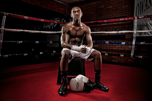 A dark-skinned boxer is sitting in the ring